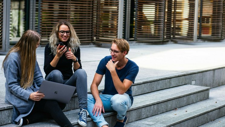 Kolm noort istuvad trepil ning vestlevad omavahel, ühel on käes telefon, teisel sülearvuti